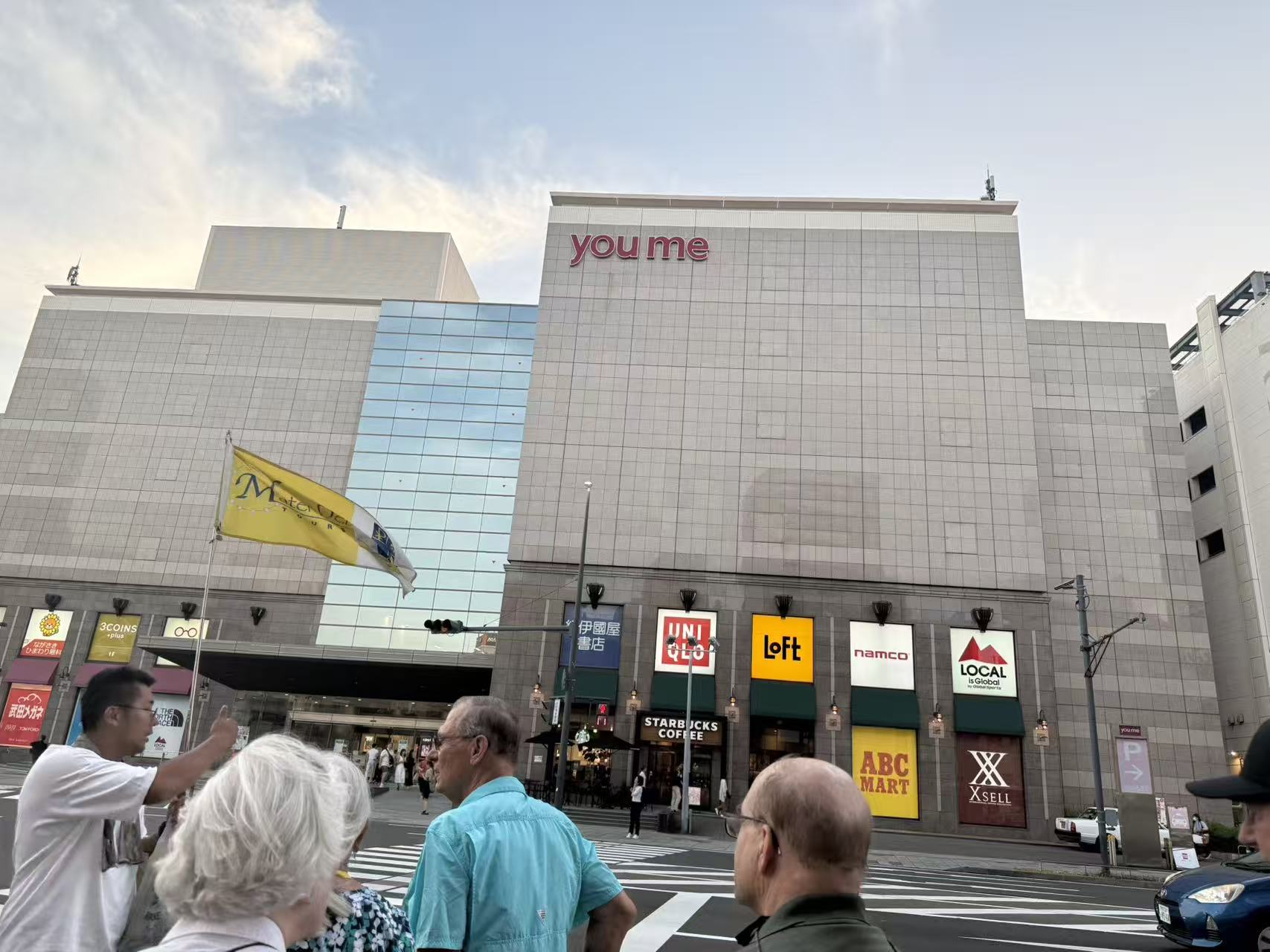 Pilgrims crossing a city street beside a Japanese shopping center